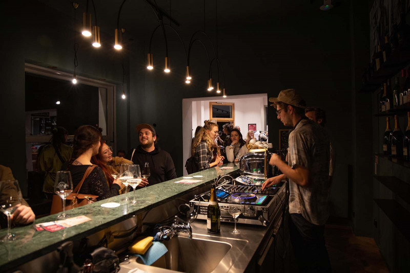 Stimmungsvolle Abendveranstaltung bei ‚Bubbles & Beats‘ in Saffer’s WinzerWelt mit DJ an der Bar und Gästen bei Wein und Musik im gemütlichen Ambiente.